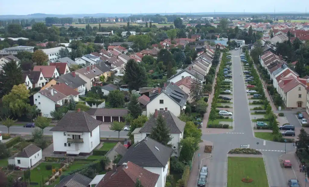 Luftaufnahme eines Vorstadtviertels mit Häuserreihen, grünen Rasenflächen und geparkten Autos entlang der Straße.
