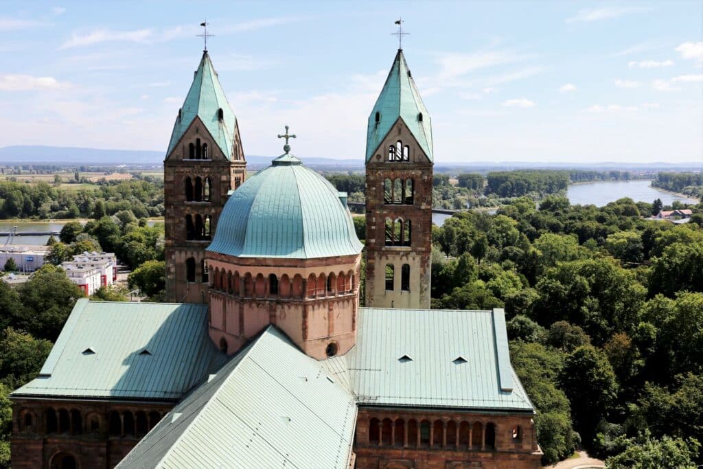 Luftaufnahme des majestätischen Speyerer Doms mit seinen ikonischen Zwillingstürmen und einer großen Kuppel, eingebettet in üppiges Grün und flankiert von einem ruhigen Fluss, so nahtlos wie ein gut gefertigtes Garagentor.