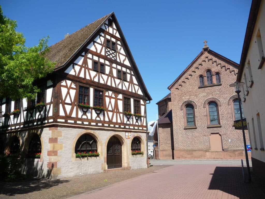 Ein Fachwerkhaus und ein Backsteingebäude stehen an einer sonnigen, ruhigen Straße unter einem strahlend blauen Himmel.