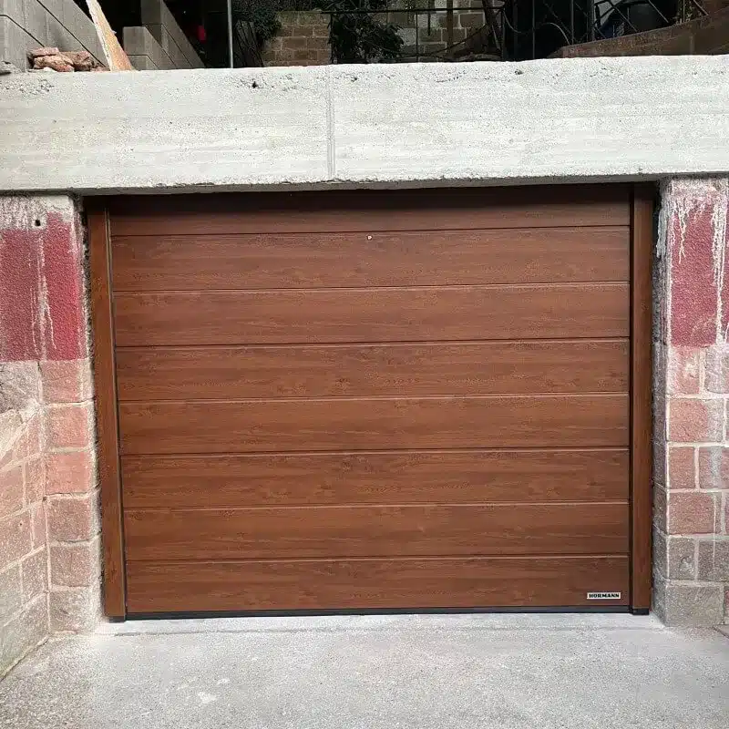 Braunes Garagentor aus Holz in einer Mauer aus Beton und Ziegeln mit roter Farbe auf den Ziegeln.