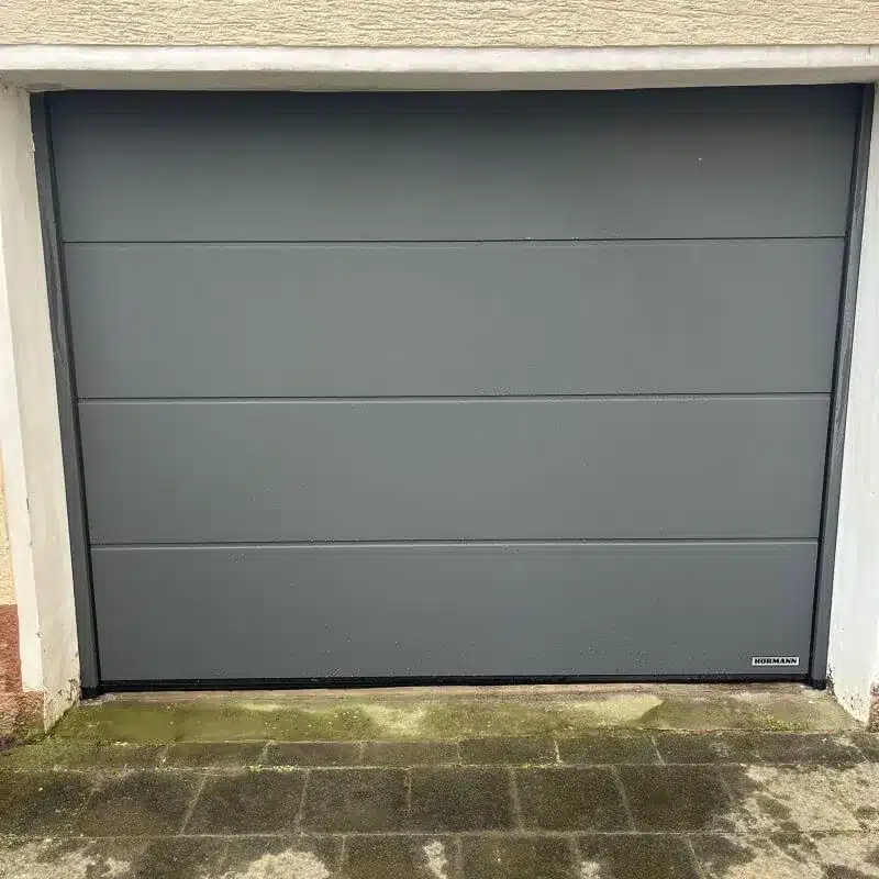 Graues, getäfeltes Garagentor mit einem kleinen Herstelleretikett in der rechten unteren Ecke.